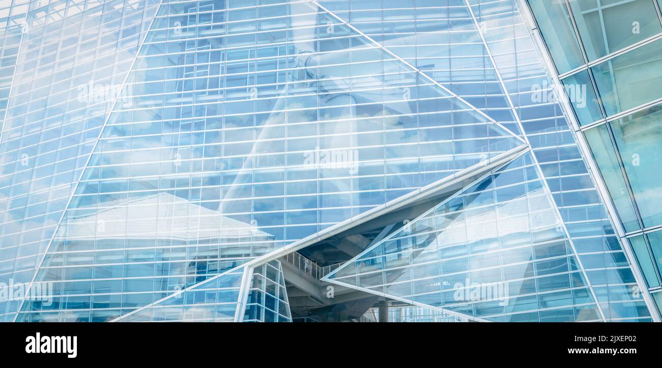 Sustainable glass building and wind power concept. Wind turbine and blue sky reflect on sustainable corporate office building. Green energy. Stock Photo