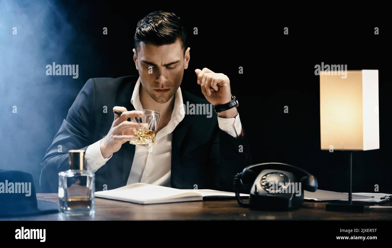 Businessman holding whiskey near notebook and telephone on black background with smoke,stock image Stock Photo