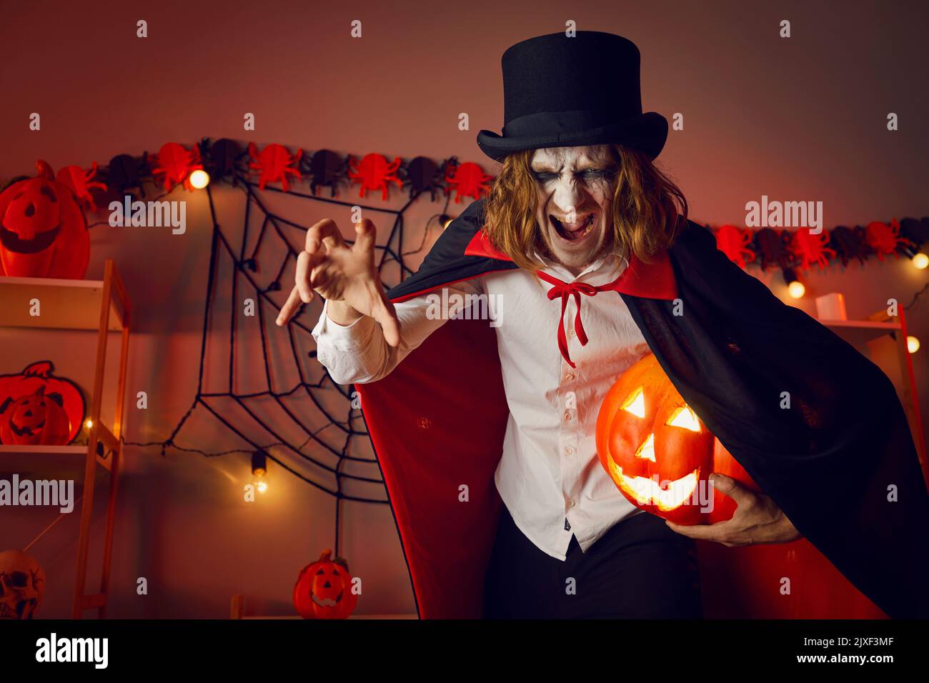 Man dressed up in costume of spooky evil vampire holding jack-o-lantern and hissing Stock Photo