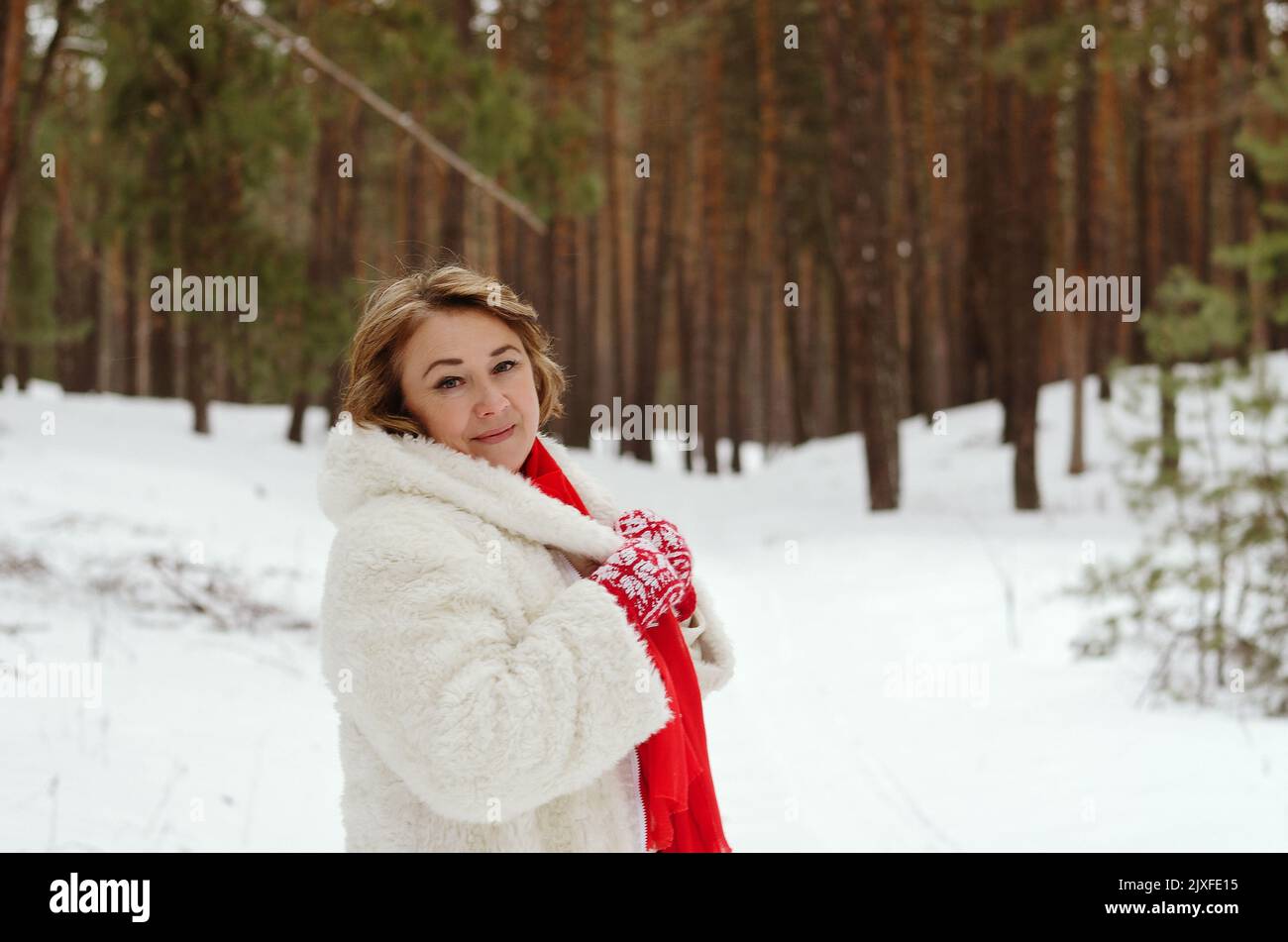 funny old woman in jeans, white hat and jacket in snowy park, forest. Mother walking near snow covered pine trees.  Having fun. Family winter Stock Photo