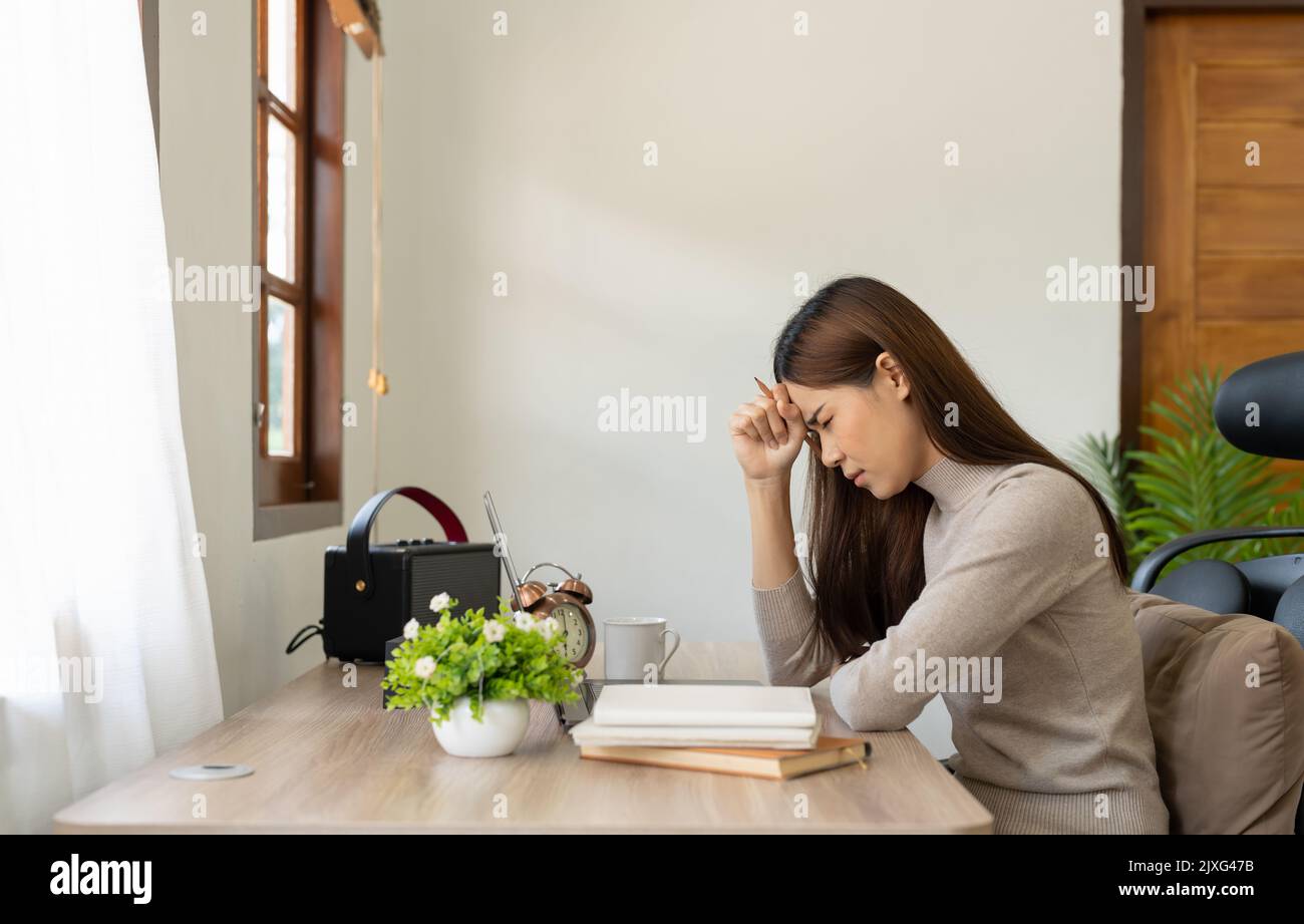 Young asian Woman Feels Sudden Burst of Pain, Headache, Migraine. Overworked Accountant Feeling Project Pressure, Stress, Massages Her Head, Temples. Stock Photo