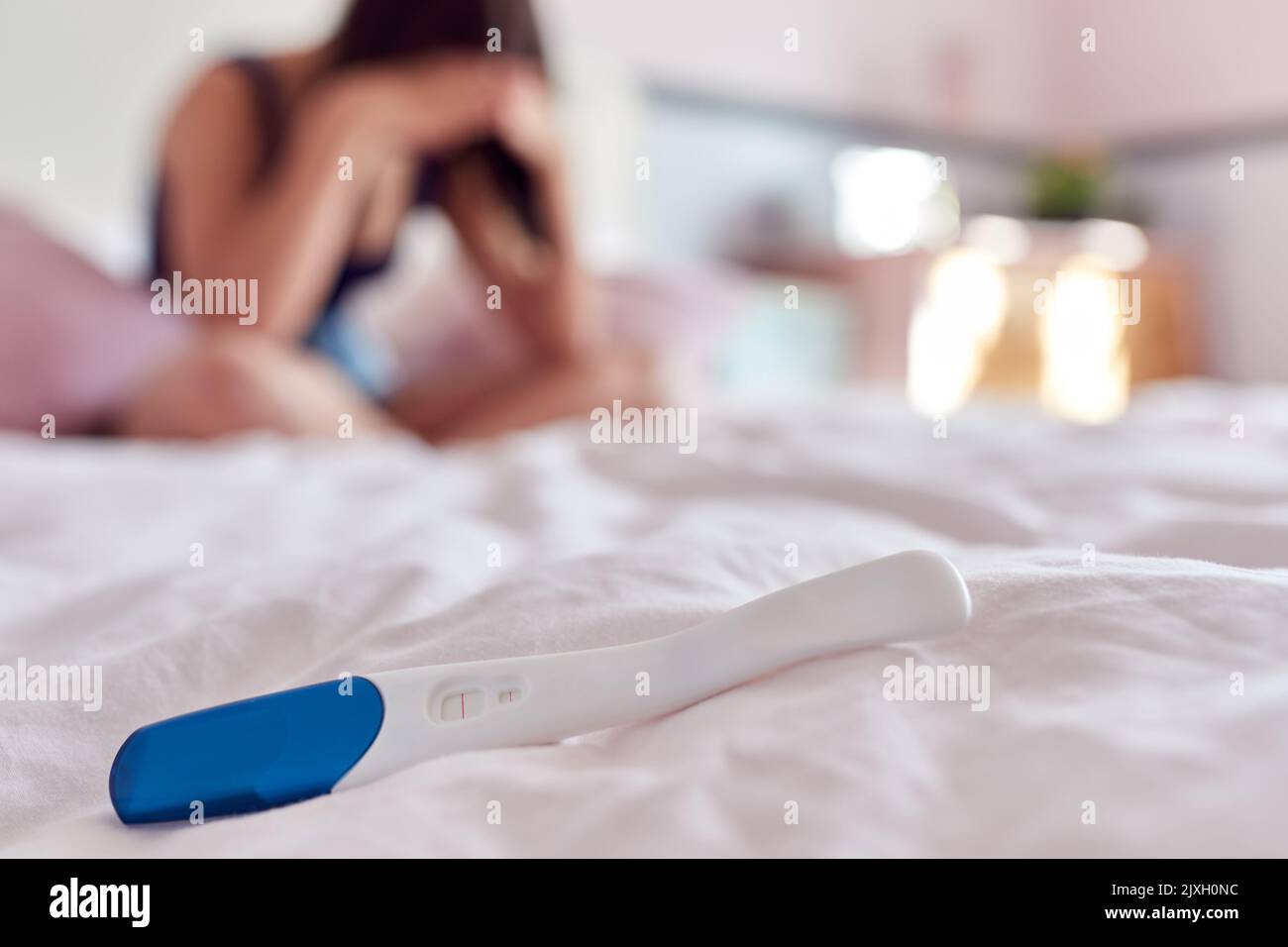 Teenage Girl Sitting On Bed With Head In Hands And Positive Pregnancy