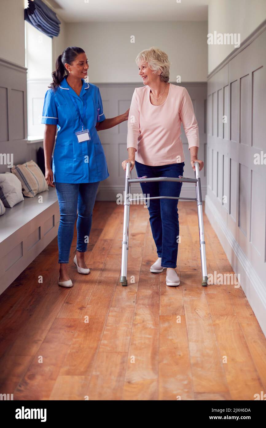Senior Woman At Home Using Walking Frame Being Helped By Female Care Worker In Uniform Stock Photo