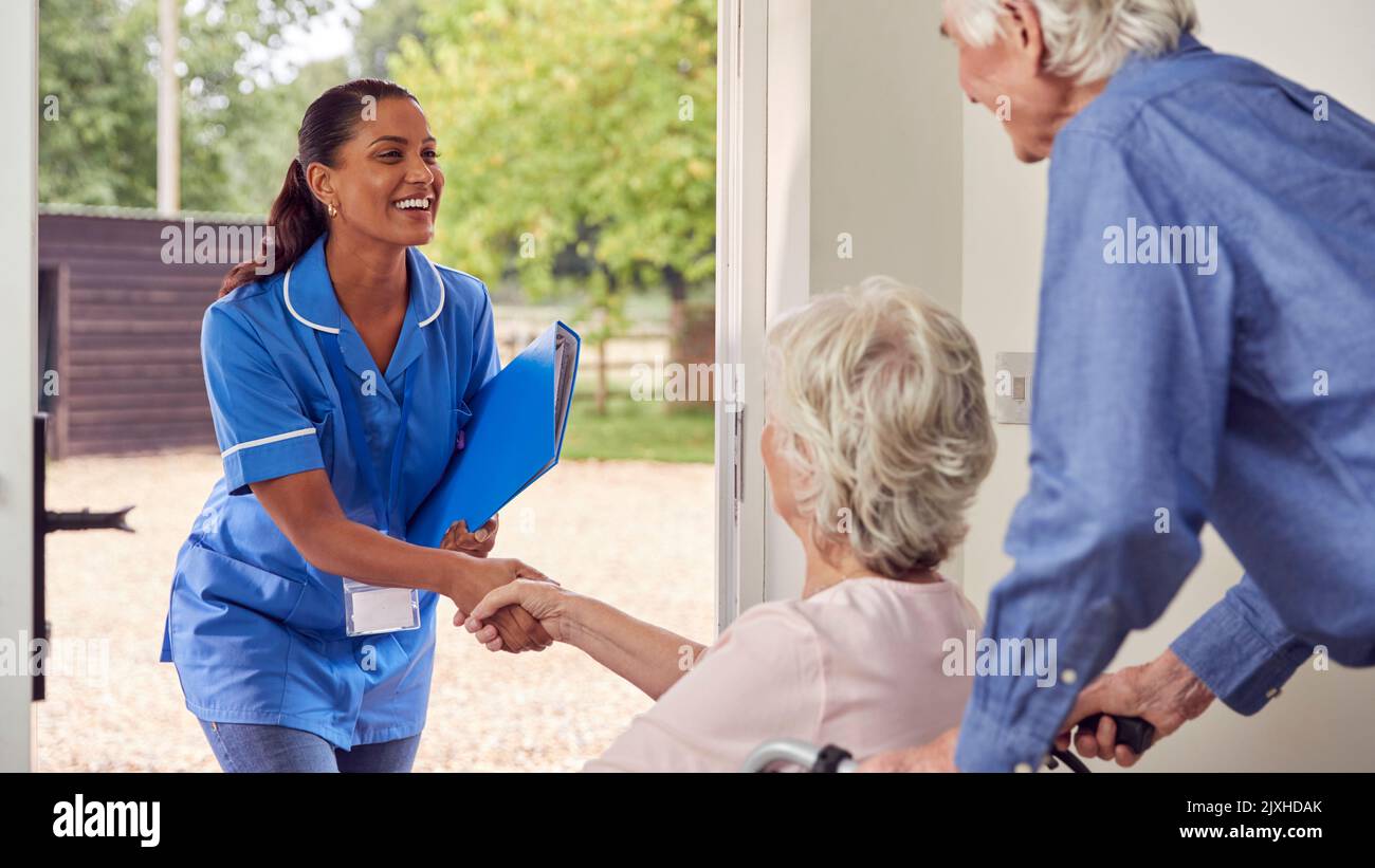 Senior Couple With Woman In Wheelchair Greeting Nurse Or Care Worker Making Home Visit At Door Stock Photo
