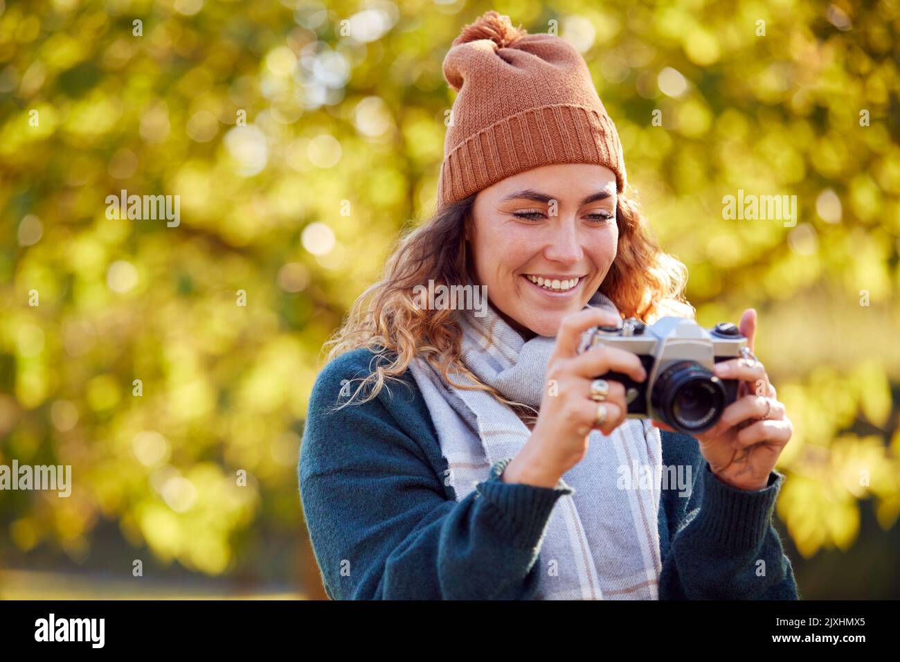 Woman In Autumn Countryside Taking Photo On Retro Style Digital Camera To Post To Social Media Stock Photo