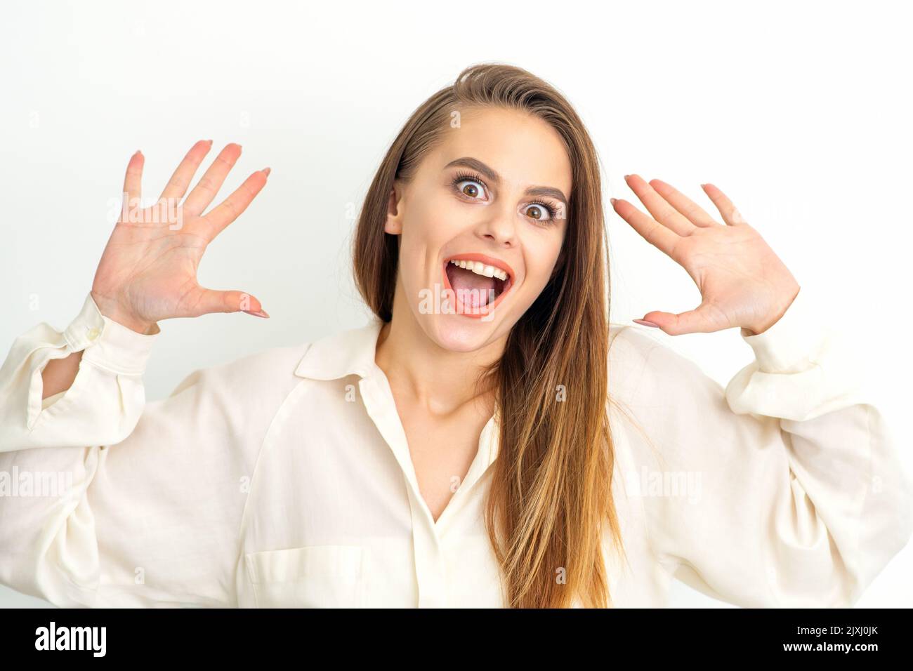 Portrait of young caucasian woman wearing white shirt raises hands and ...