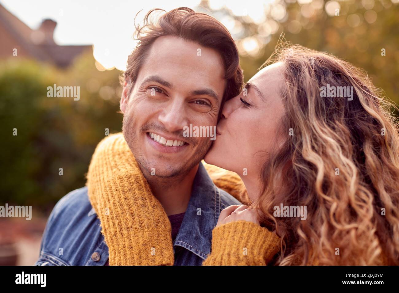 Portrait Of Happy Loving Couple With Woman Giving Man Kiss On The Cheek Stock Photo