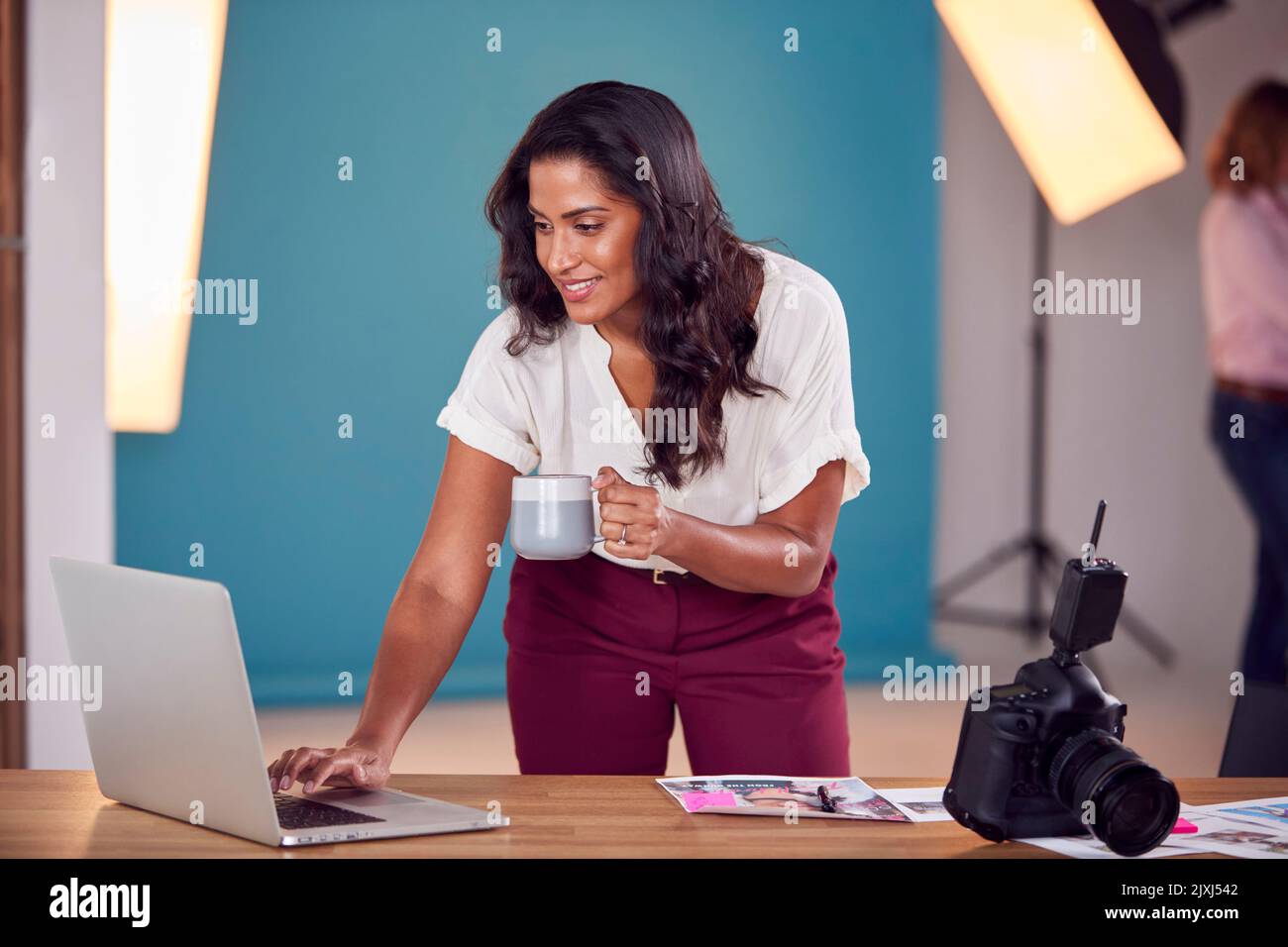 Mature Female Photographer Checking Images On Laptop During Shoot In Studio Stock Photo