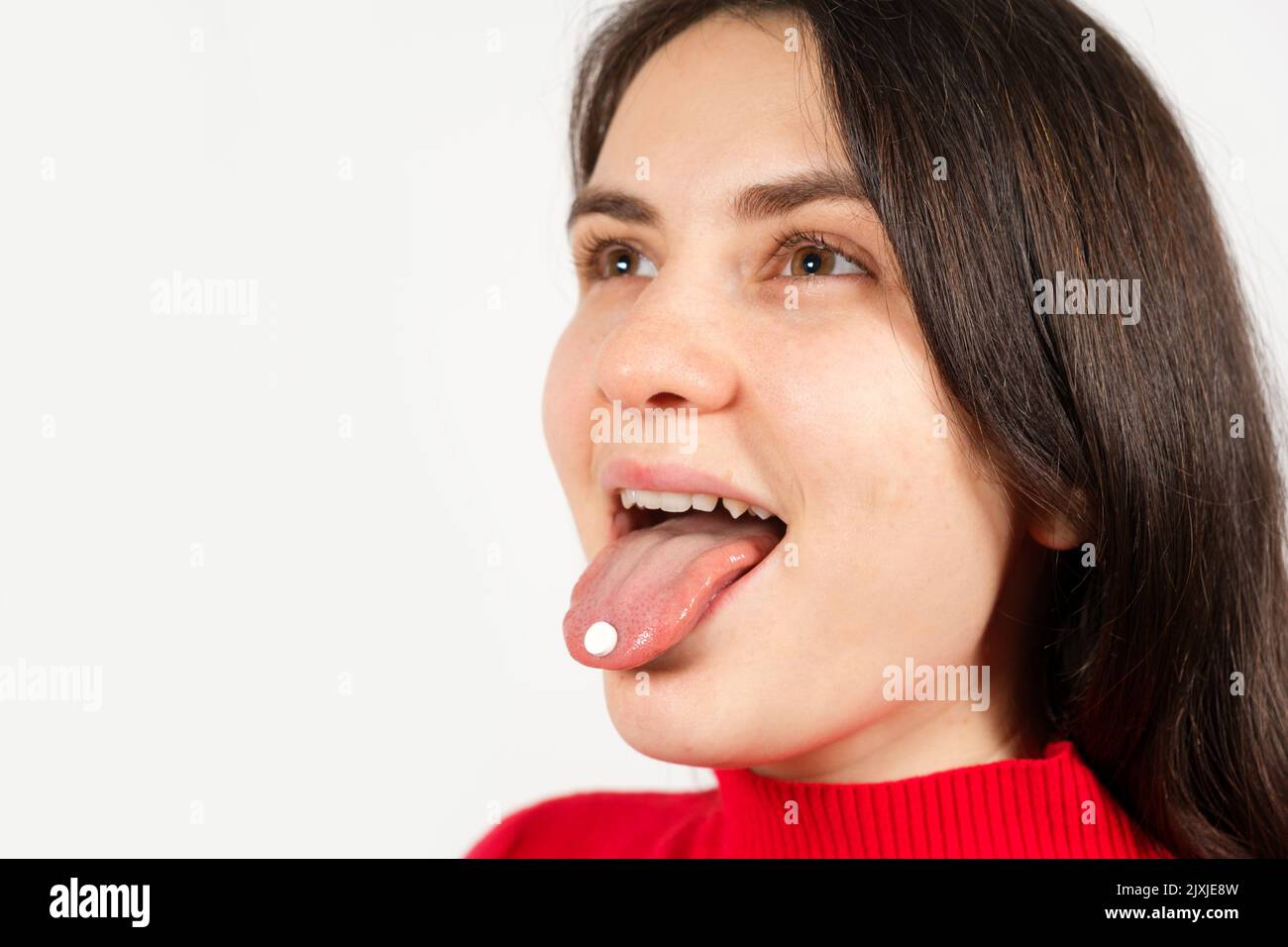 Woman with open mouth with pills on tongue on white background with