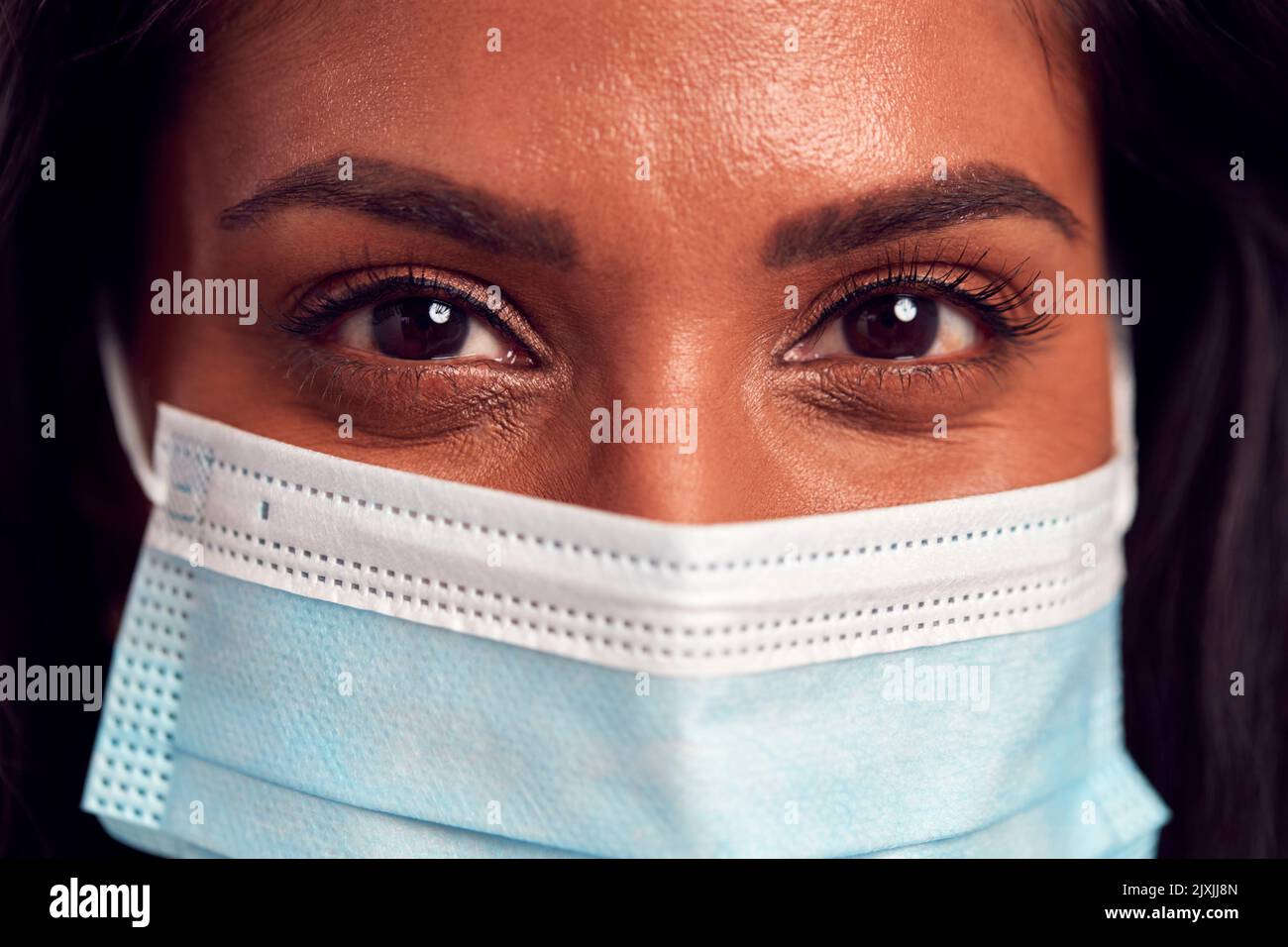 Close Up Portrait Of Female Mature Woman Wearing Face Mask In Front Of Blue Studio Background Stock Photo