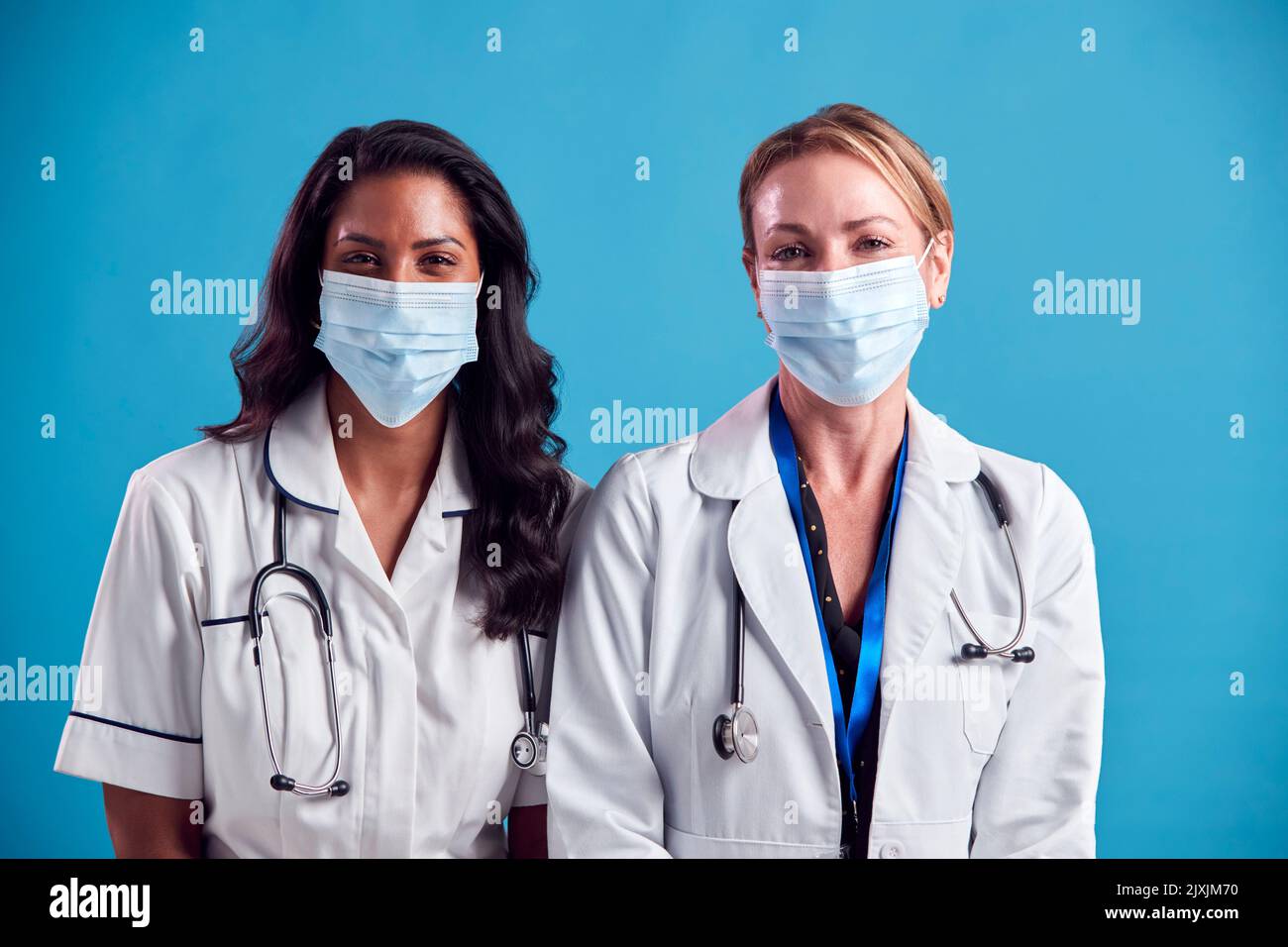 Portrait Of Female Doctor And Nurse Wearing Face Masks Standing In Front Of Blue Studio Background Stock Photo