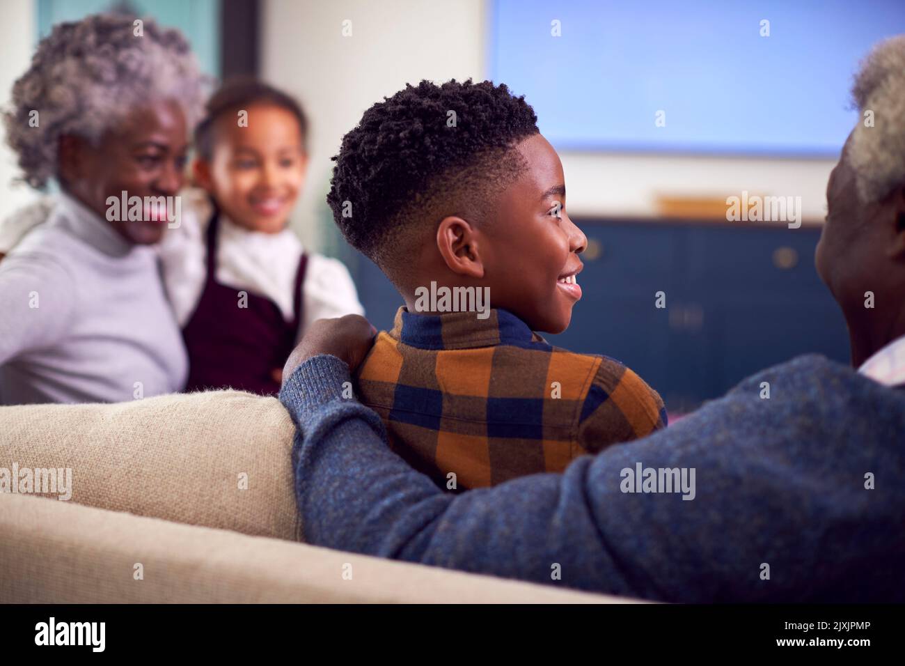 Rear View Of Grandparents With Grandchildren Sitting On Sofa Watching Movie On TV At Home Stock Photo