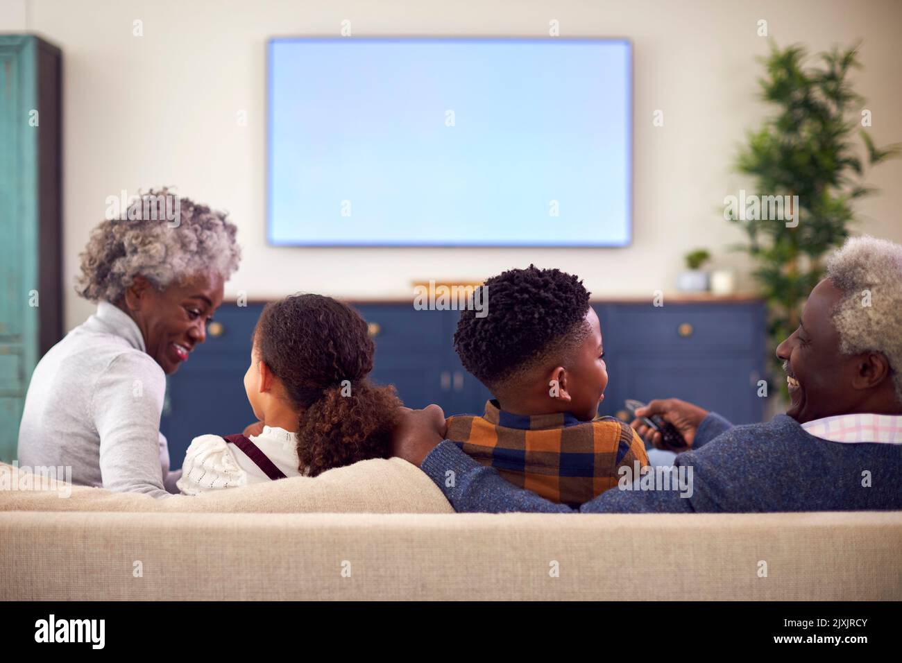 Rear View Of Grandparents With Grandchildren Sitting On Sofa Watching