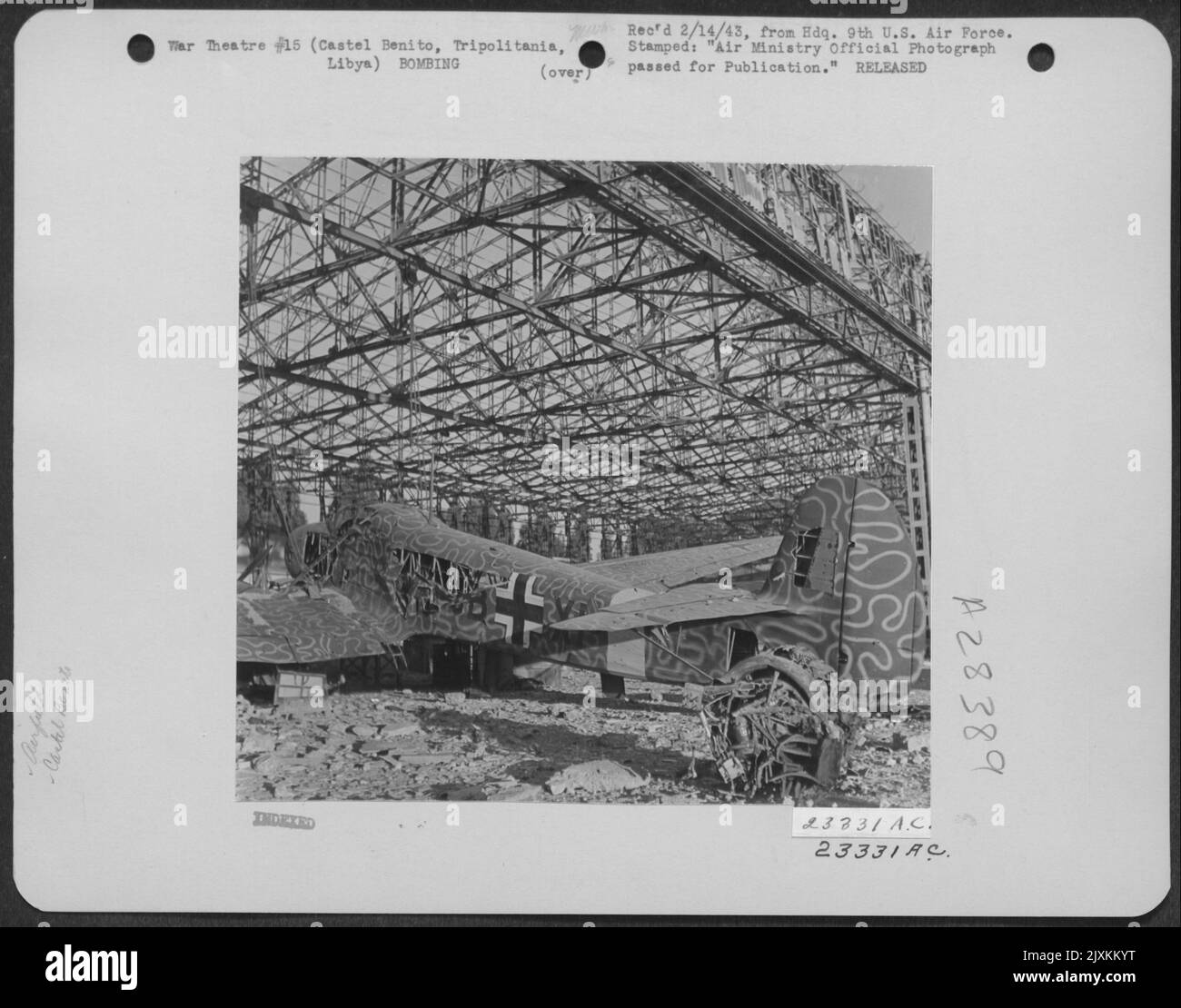 The wreck of a strangely camouflaged Focke Wulf FW 58 trainer stands beside the skeleton of a hangar on the airfield at Castel Benito, Tripolitania, Libya. 26 January 1943. Stock Photo