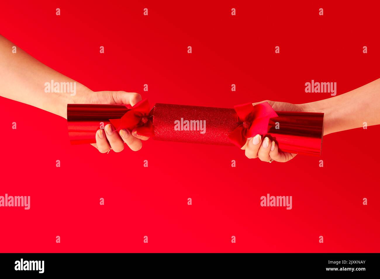 Close Up Studio Shot Of Female Hands Pulling Christmas Cracker Against Red Background Stock Photo