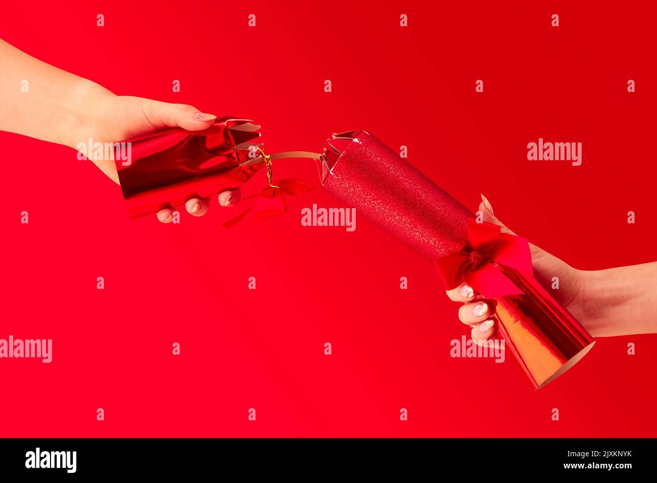Close Up Studio Shot Of Female Hands Pulling Christmas Cracker Against Red Background Stock Photo