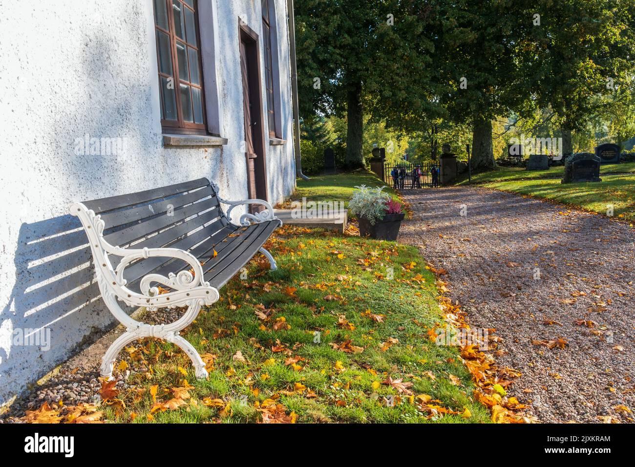 Park bench by a church and fallen autumn leaves Stock Photo