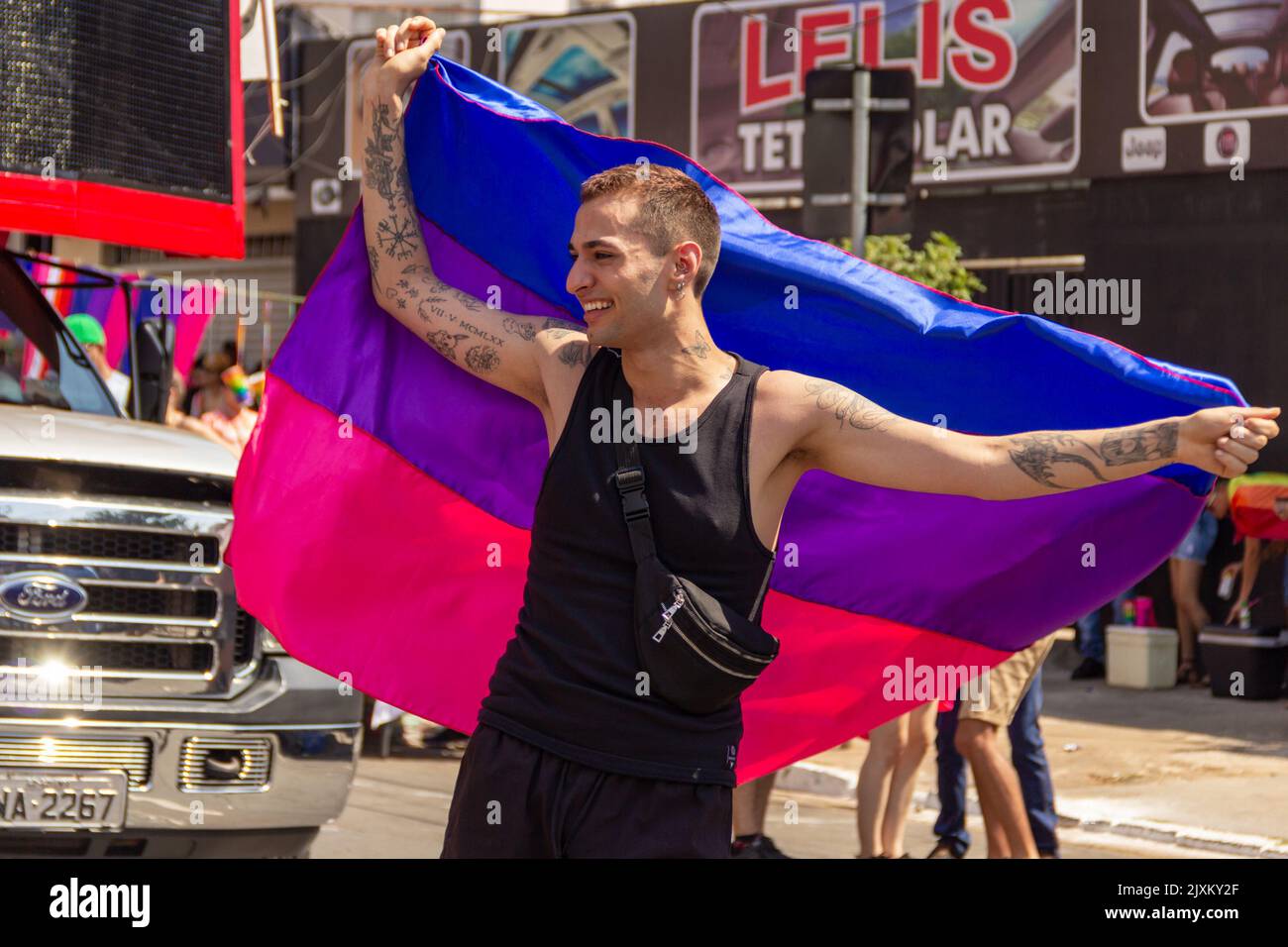 Goiânia, Goias, Brazil – September 04, 2022: A young man with a blue, purple and pink flag, happily dancing with open arms. Photo LGBTQIA+ Parade. Stock Photo