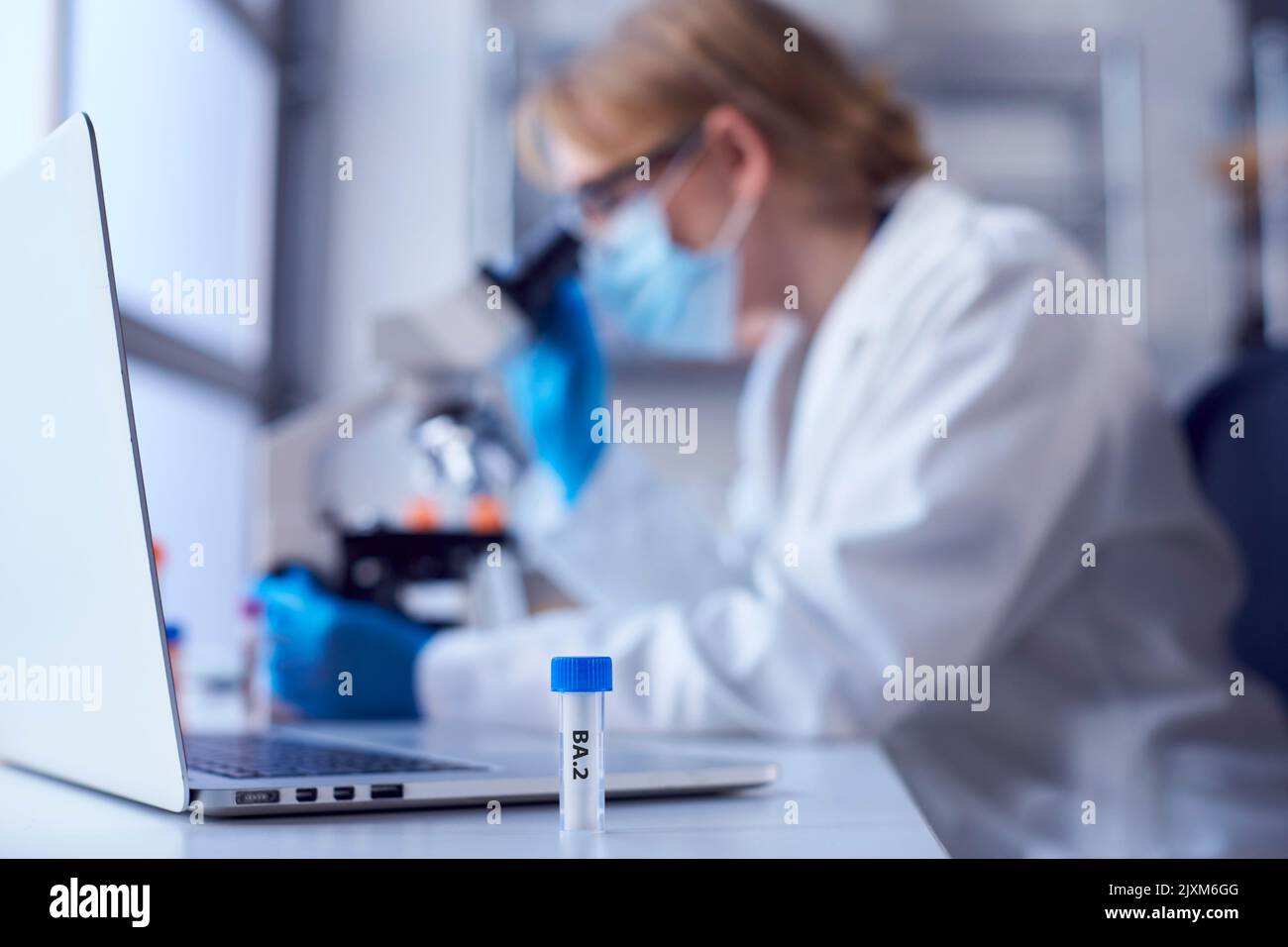 Female Lab Research Worker Wearing PPE Holding Test Tube Labelled BA.2 Stock Photo