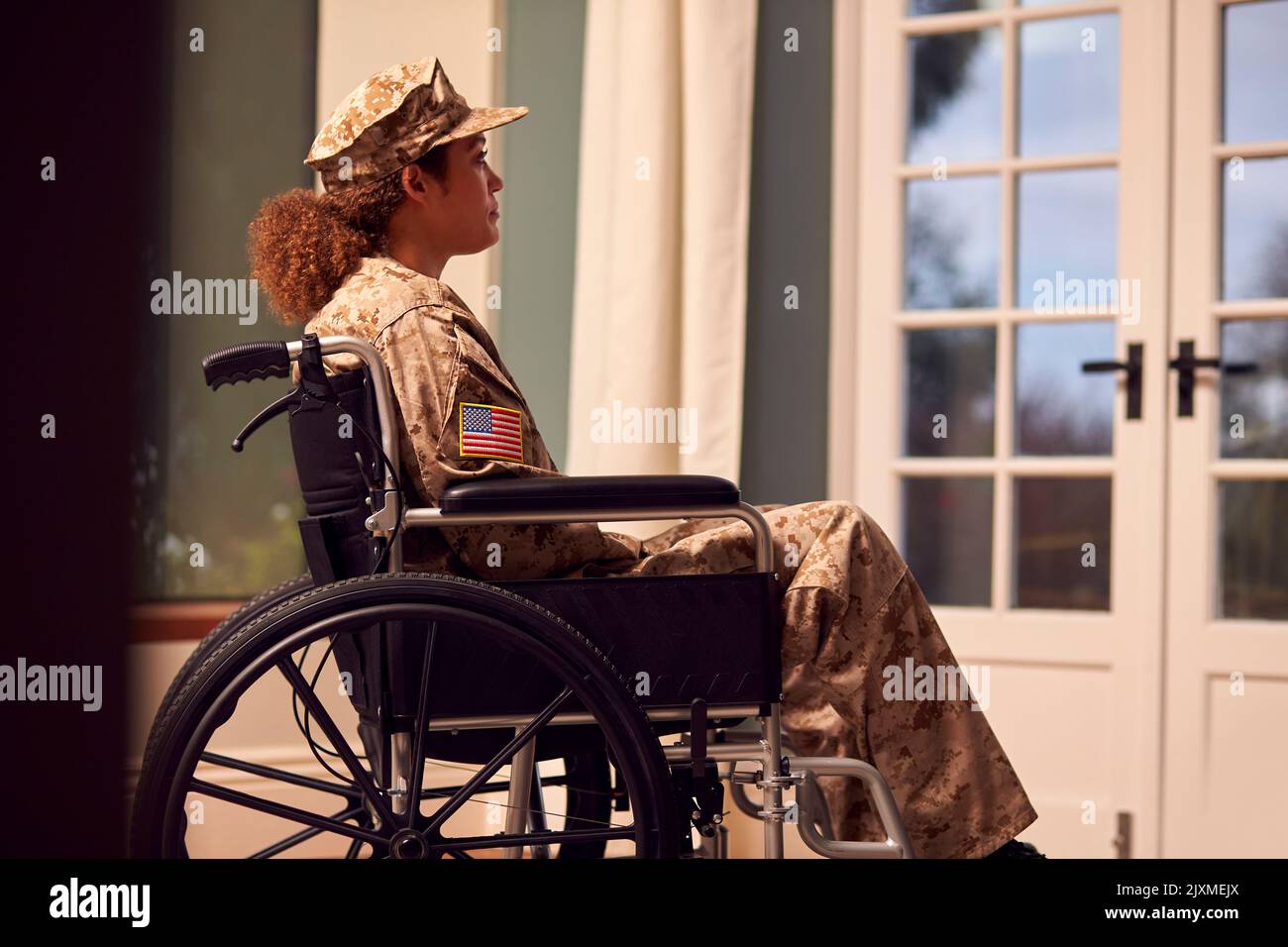 Injured Female American Soldier Wearing Uniform Sitting In Wheelchair Looking Out Of Window Stock Photo