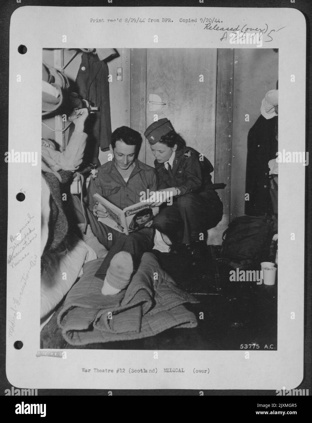 Pvt. Joseph Mencas, of Farmington, W.Va., scans a magazine during this flight back to the U.S. aboard an ATC plane. Lt. Geraldine E. Lyane of St. Paul, Minn., the fligth nurse in charge of the wounded men, propped up Pvt. Mencas' injured foot on a Stock Photo