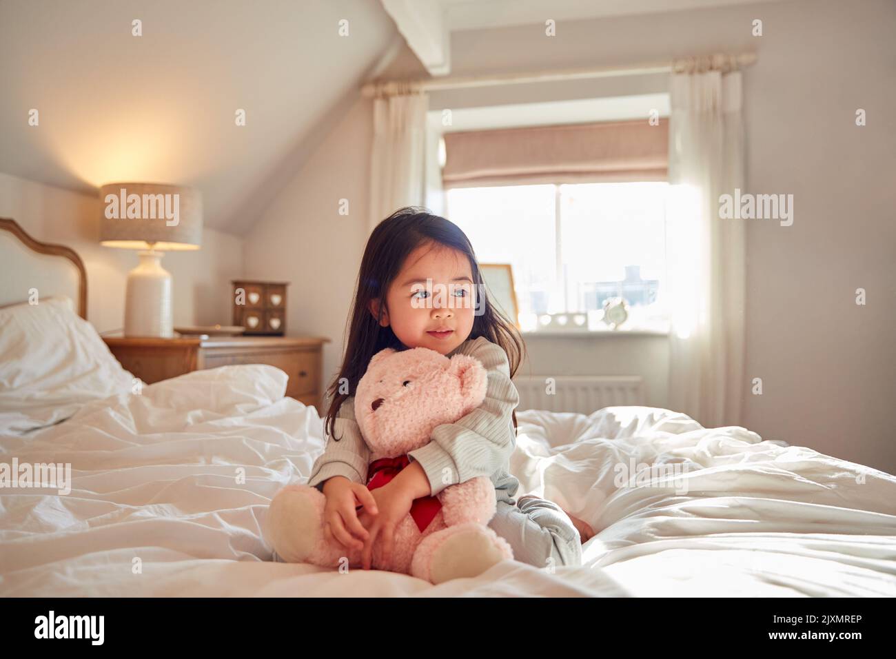 Young Girl Sitting On Bed Wearing Pyjamas At Home Cuddling Soft Toy Stock Photo