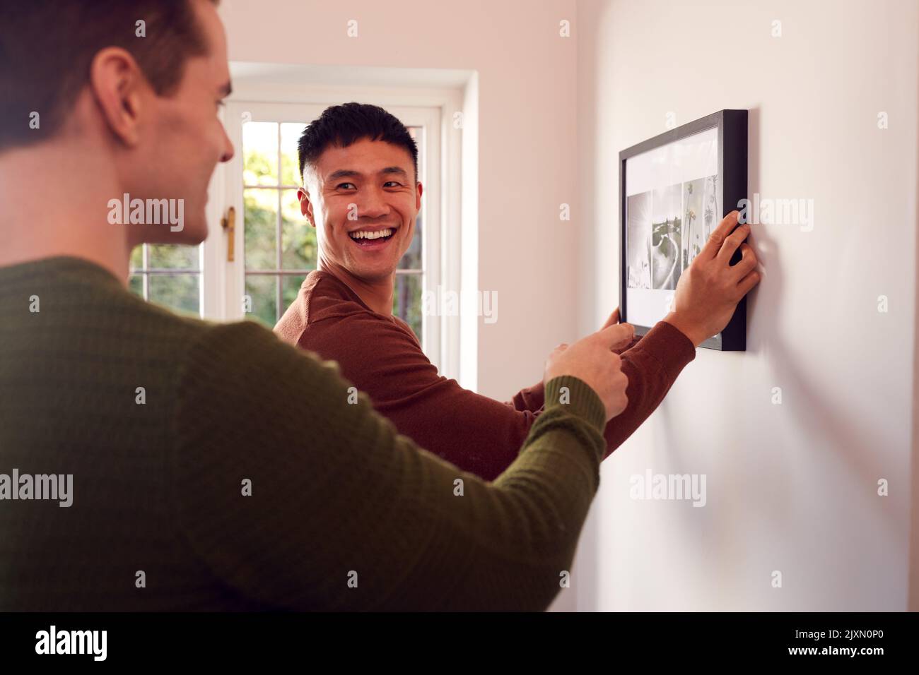 Same Sex Male Couple Hanging Picture On Wall At Home Together Stock Photo