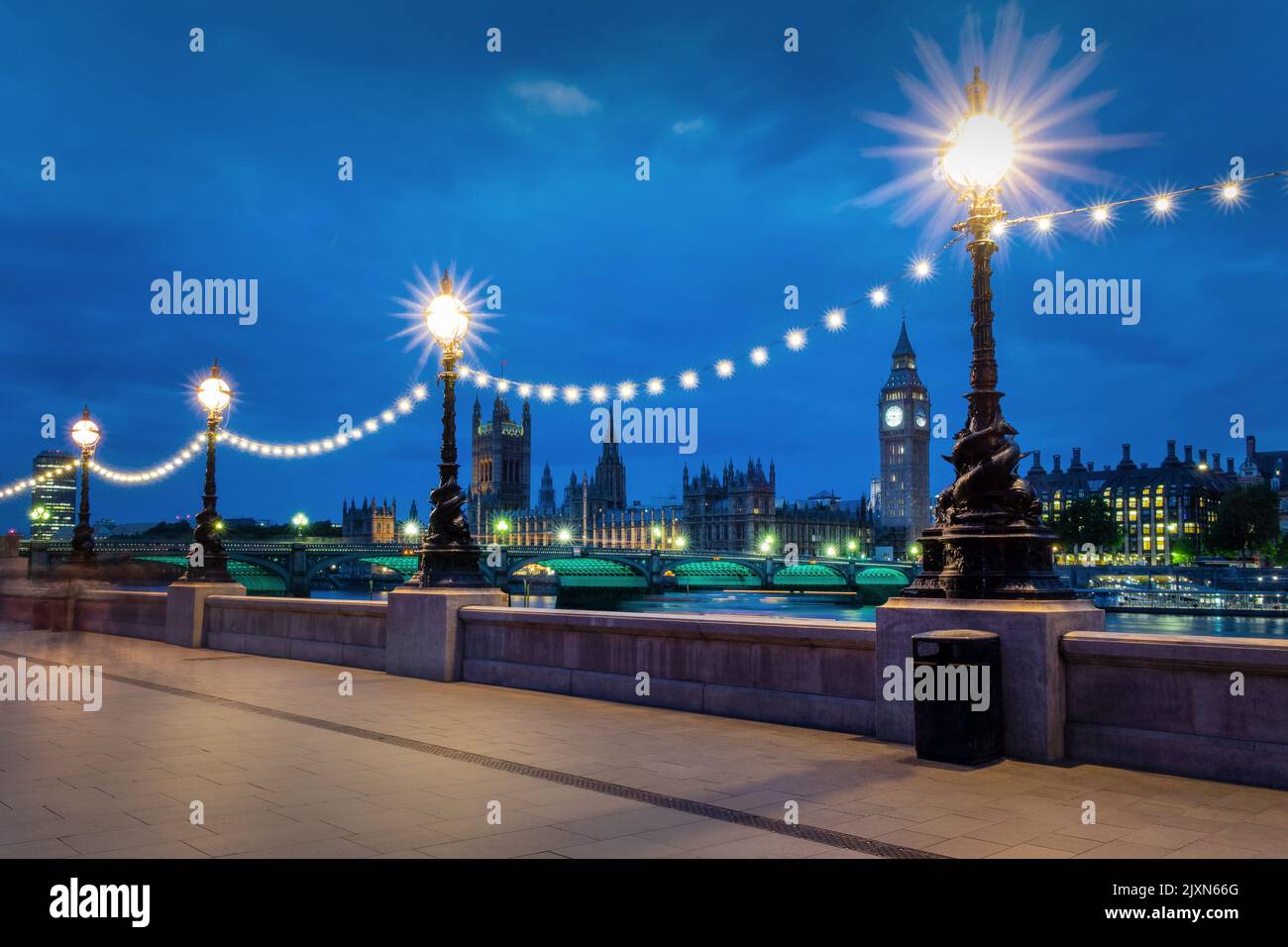 Lampposts illuminated at night on the Queen's Walk, view on Westminster palace and Big Ben in London, UK Stock Photo