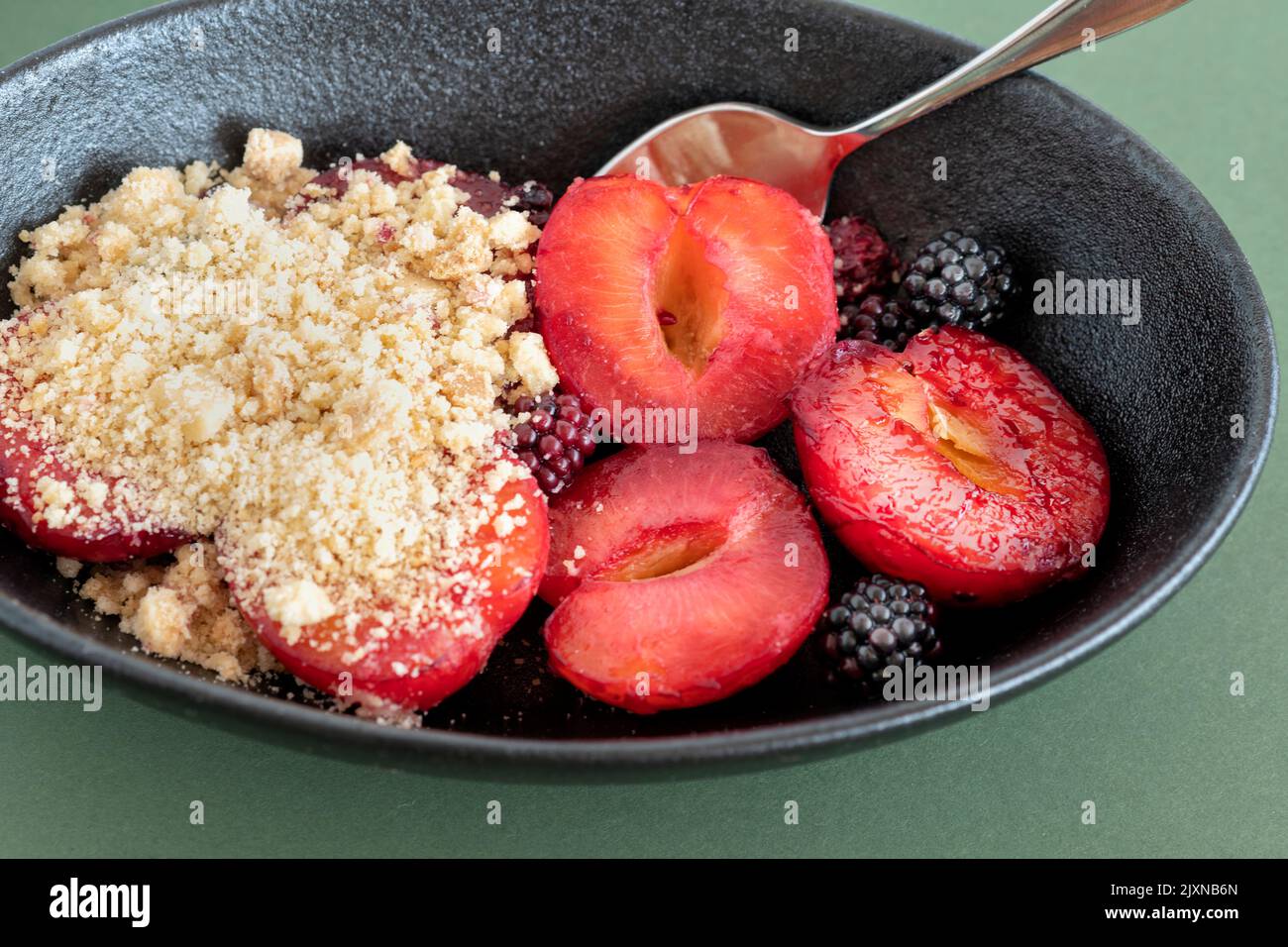 A traditional English plum and blackberry fruit crumble desert. The pudding is served hot with the usual flour based crumble mixture Stock Photo