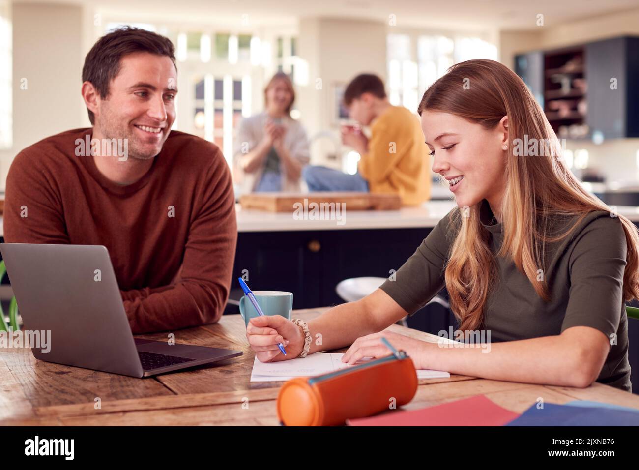 Father Helping Teenage Daughter With Homework Sitting At Kitchen Table ...