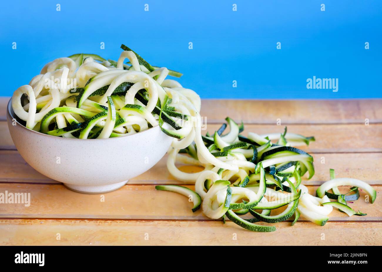 A bowl filled, and spilling over, with raw spiralized courgette or zucchini. Used as a Keto diet alternative to spaghetti and known as courgetti Stock Photo
