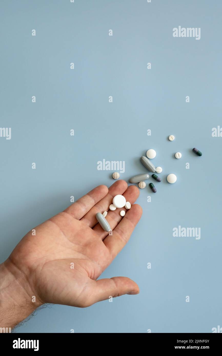 Palm with a handful of pills on a blue background. Concept of preparing for the cold season or addiction to drugs. Copy space.  Stock Photo