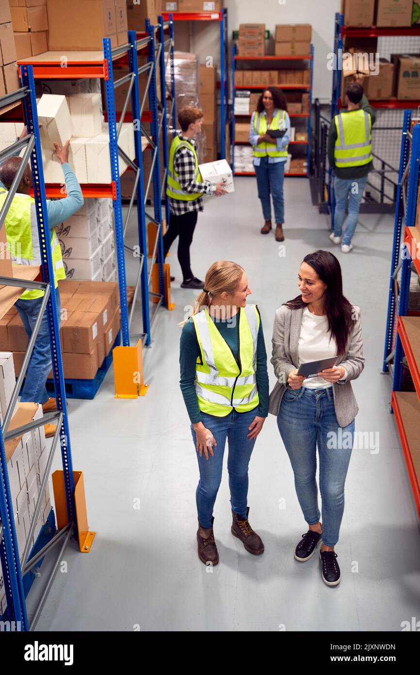 Modern Warehouse With Fulfilment Staff Picking Items From Shelves And Manager Using Digital Tablet Stock Photo