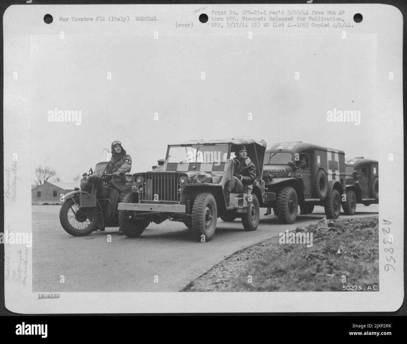 Paced by a motorcycle policeman and jeep equipped with two way radio, ambulance of a 9th US Air Force evacuation unit await arrival of troop carrier aircraft which will relay soldier patients to general hospitals several hundred miles distant. The Stock Photo