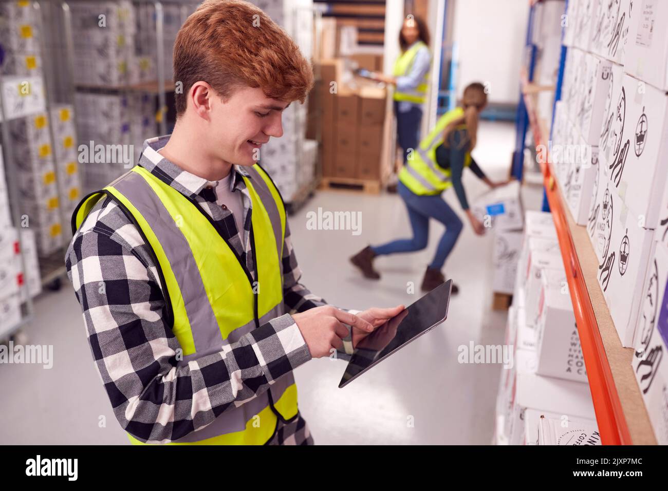 Male Worker Inside Busy Warehouse Checking Stock On Shelves Using Digital Tablet Stock Photo