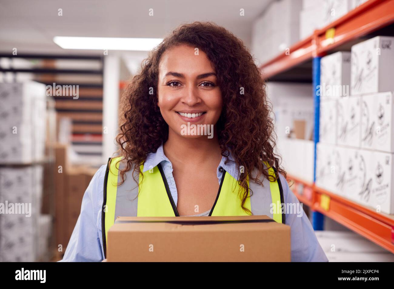 Portrait Of Female Worker Holding Box Inside Warehouse Stock Photo