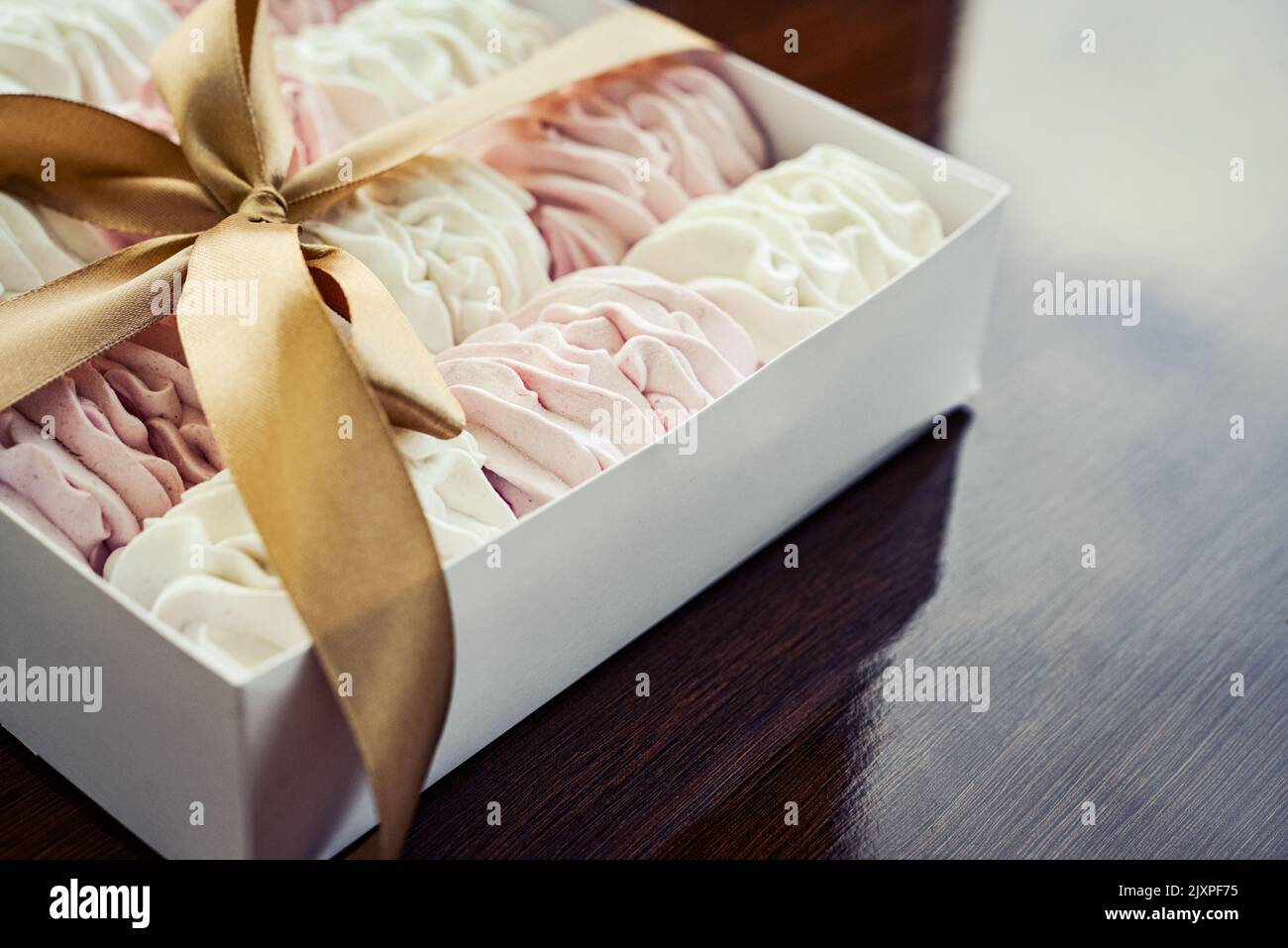 Homemade white and pink zephyr in box with bow on wooden background, top view Stock Photo