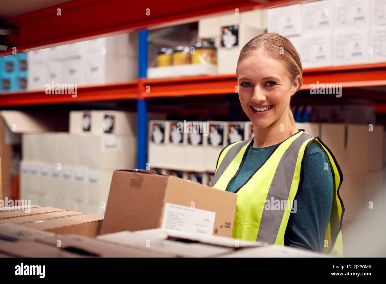 Portrait Of Female Worker Picking Box From Shelf Inside Warehouse Stock Photo
