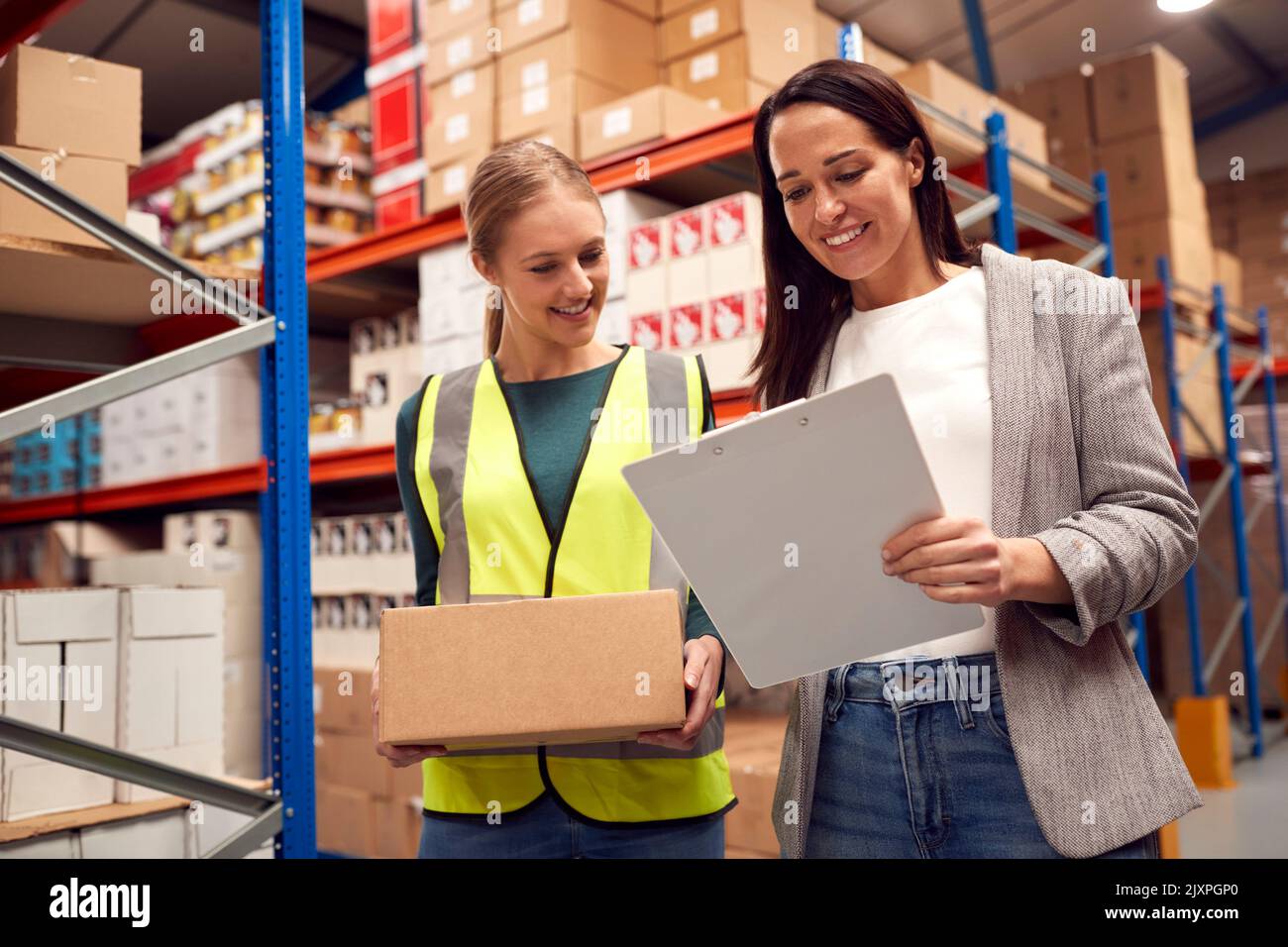 Female Team Leader With Clipboard In Warehouse Training Intern Standing By Shelves Stock Photo