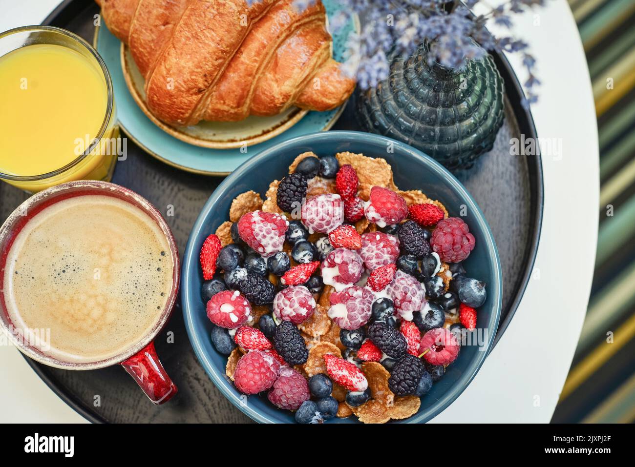 Healthy breakfast with berries, cereals and natural yogurt, coffee, orange juice, croissant on black round tray Stock Photo