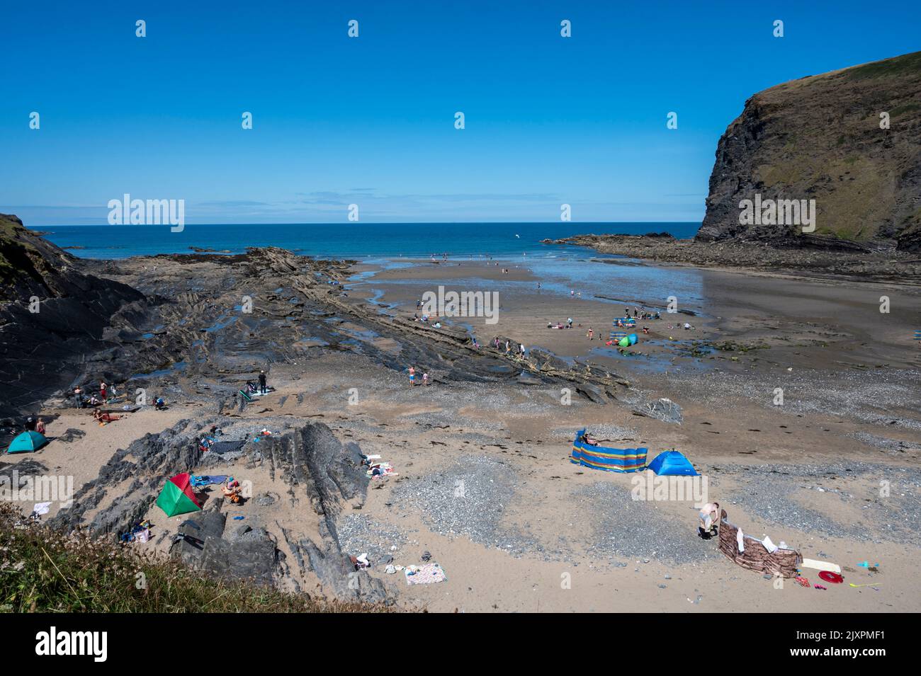 View of Crackington Haven Beach with holiday makers enjoying the sun and sea. In the background is Penkenna Point. Stock Photo