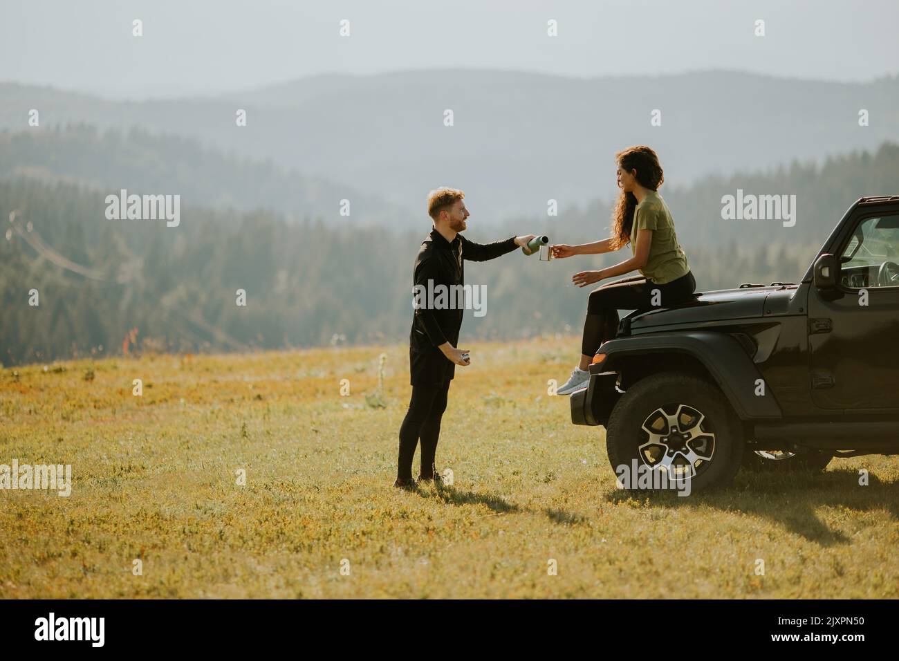 Smiling young couple preparing hiking adventure with backpacks by terrain vehicle Stock Photo
