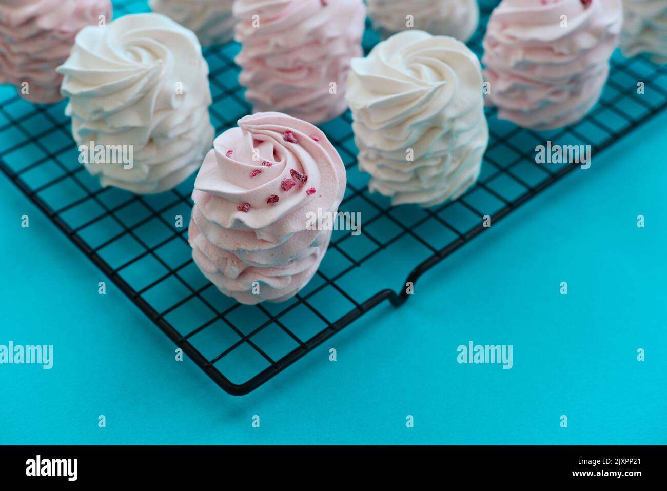 Homemade white and pink zephyr on confectionery metal grid on blue background Stock Photo