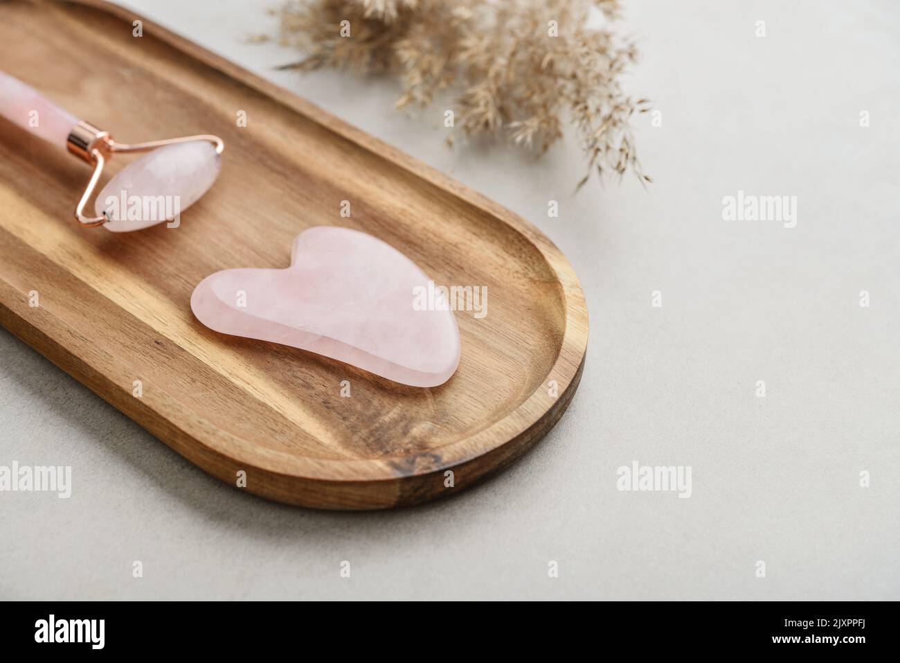 Facial rose quartz stone massage roller and gua sha massager made from natural stone on light concrete background, top view Stock Photo
