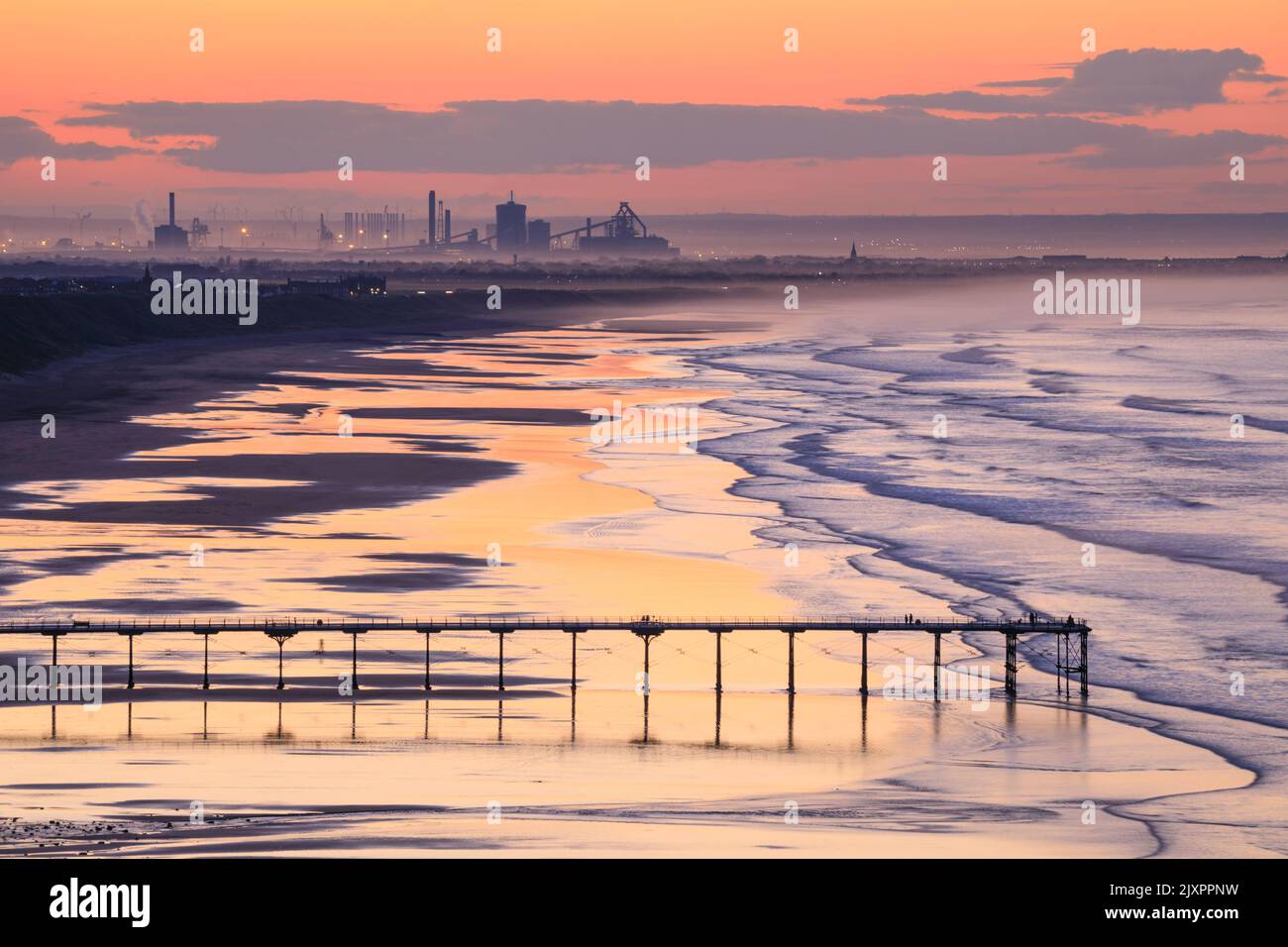 Saltburn Pier captured shortly before sunset from the coast path near Saltburn-by-the-Sea with the steelworks at Redcar in the distance. Stock Photo