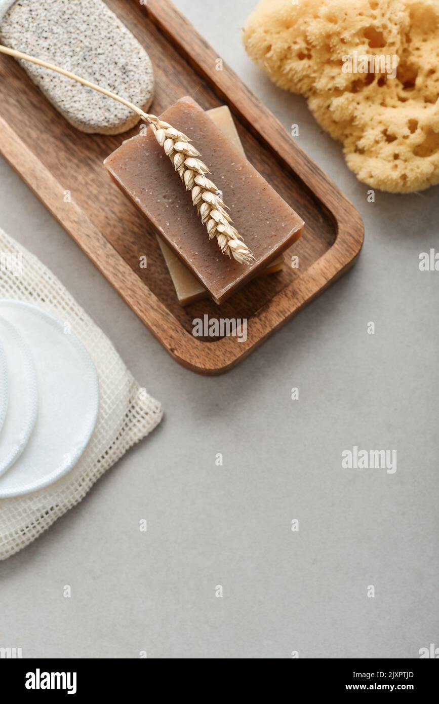Natural soap bars, wheat spikelet and pumice stone on wooden tray with various toiletries on a light concrete background, top view Stock Photo