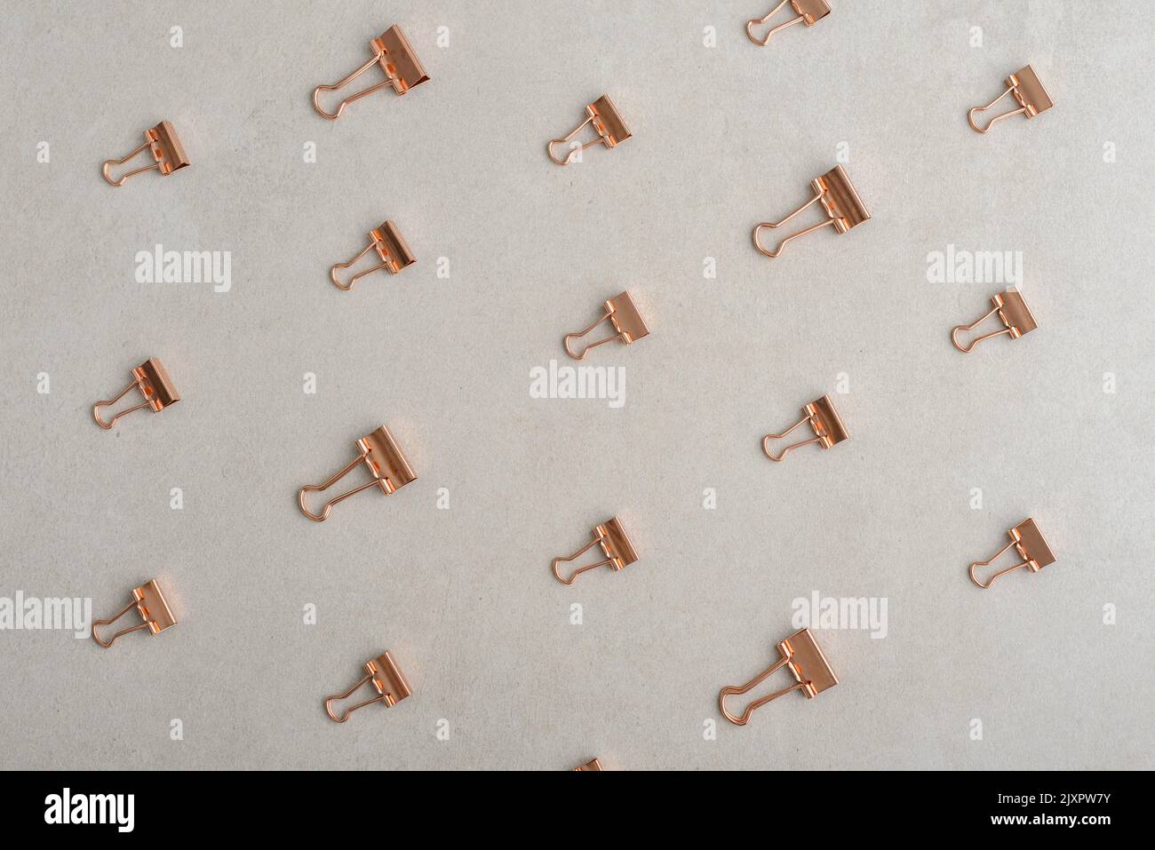 Golden paper binder clips pattern on light concrete background, top view. Office supplies background Stock Photo