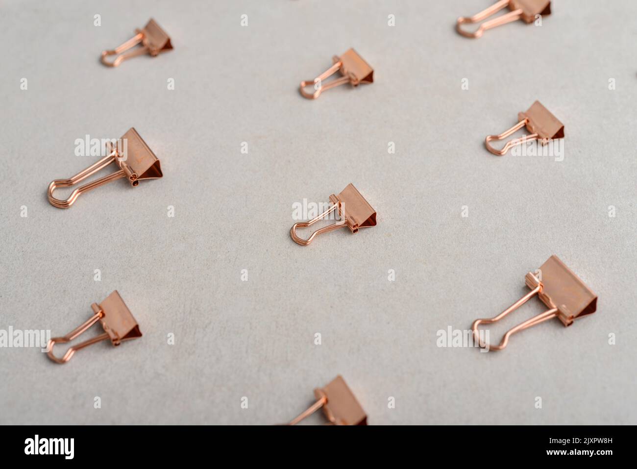 Golden paper binder clips pattern on light concrete background. Office supplies background Stock Photo