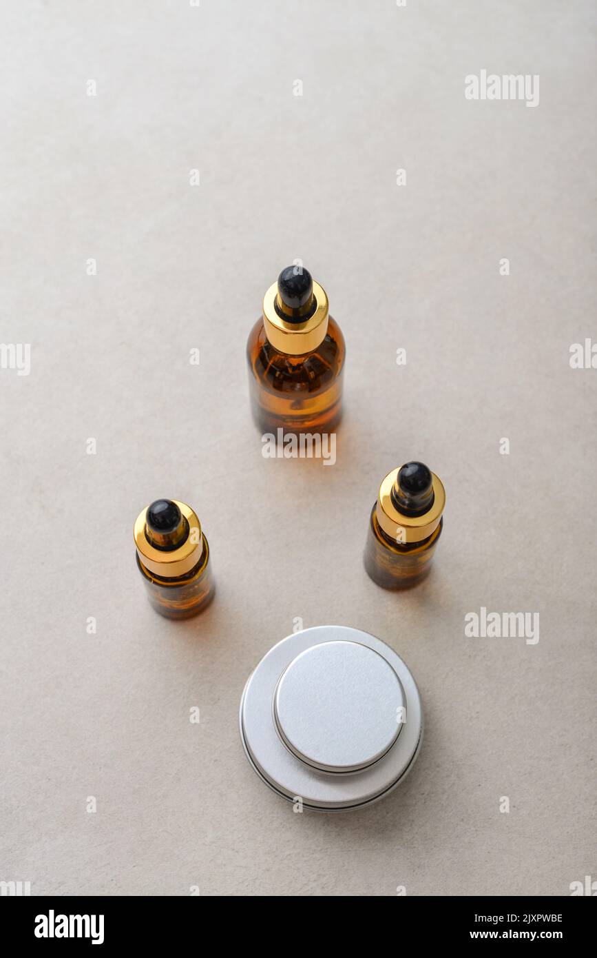 Dropper brown glass bottles, metal round tin cosmetic cans and small plastic can on light concrete background, top view Stock Photo
