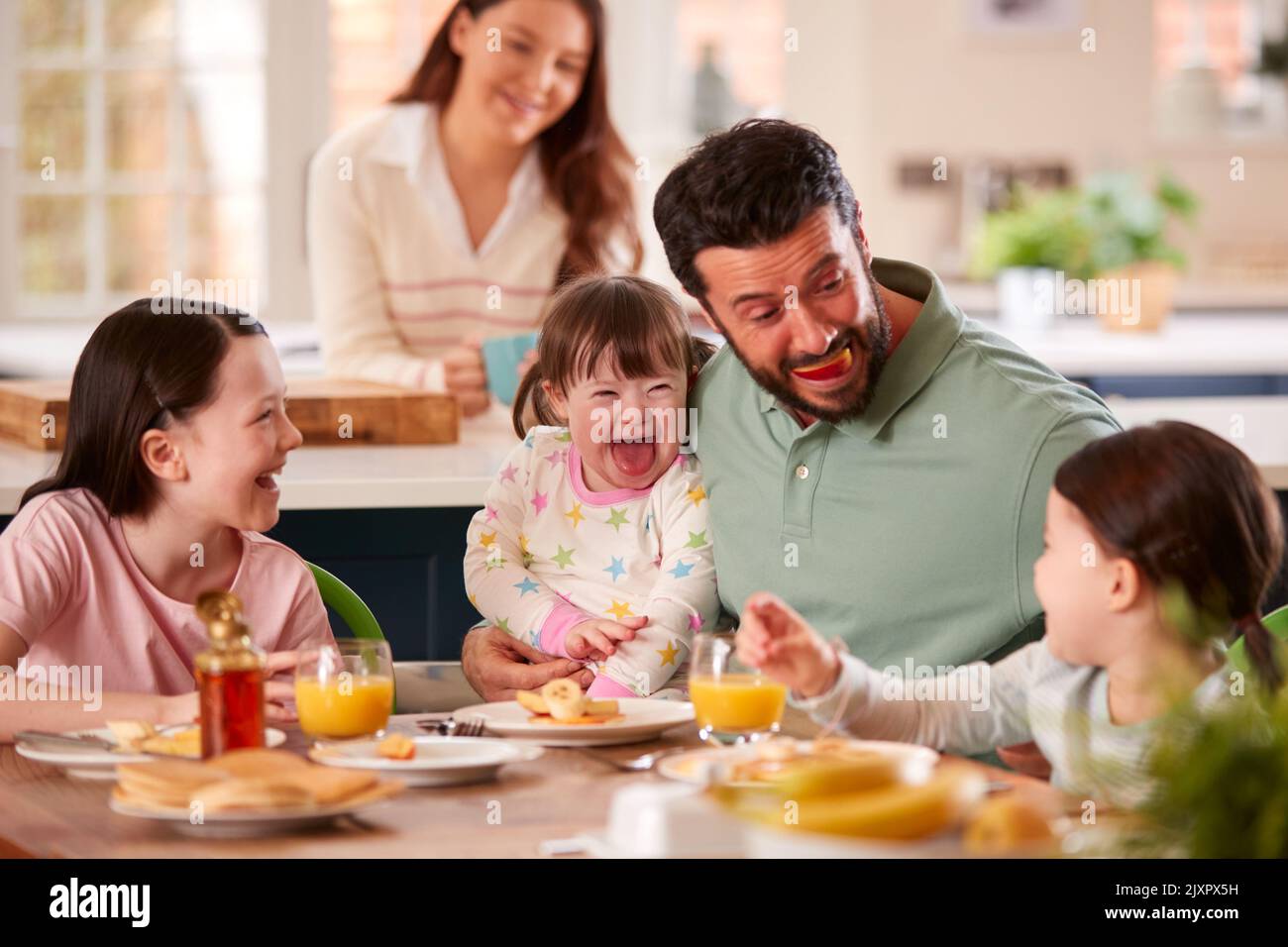 Father Making Funny Face As Family With Down Syndrome Daughter Eat Breakfast At Home Stock Photo